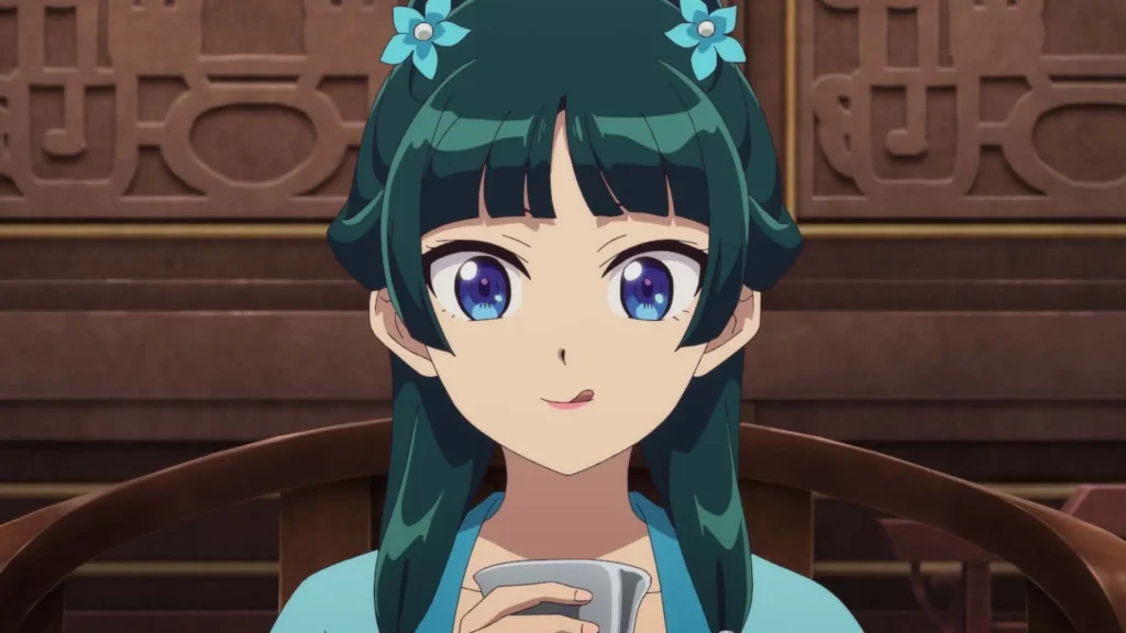 Maomao con adornos florales azules bebiendo té sentada frente a un fondo de madera tallada en el anime The Apothecary Diaries