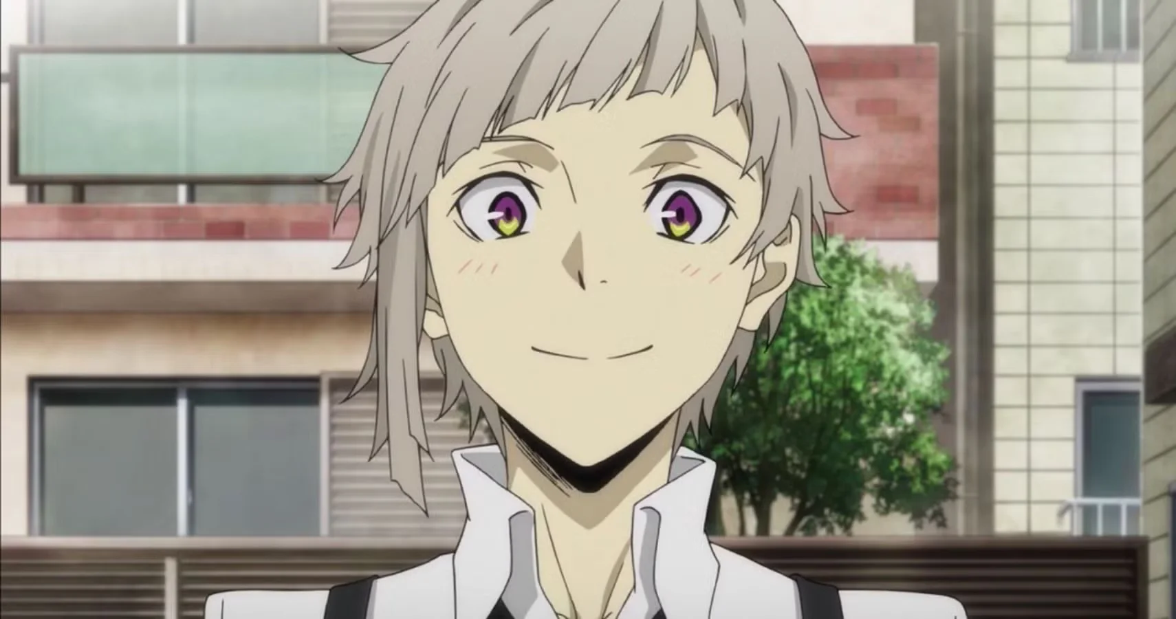 Primer plano de Atsushi Nakajima sonriendo en Bungo Stray Dogs, protagonista de la serie con sus característicos ojos bicolor, con Yokohama de fondo