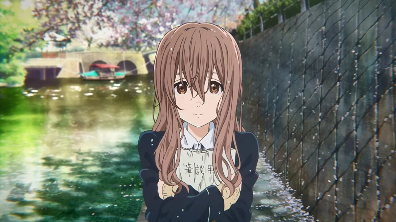 Shoko Nishimiya sosteniendo su cuaderno de comunicación junto a un canal con cerezos en A Silent Voice