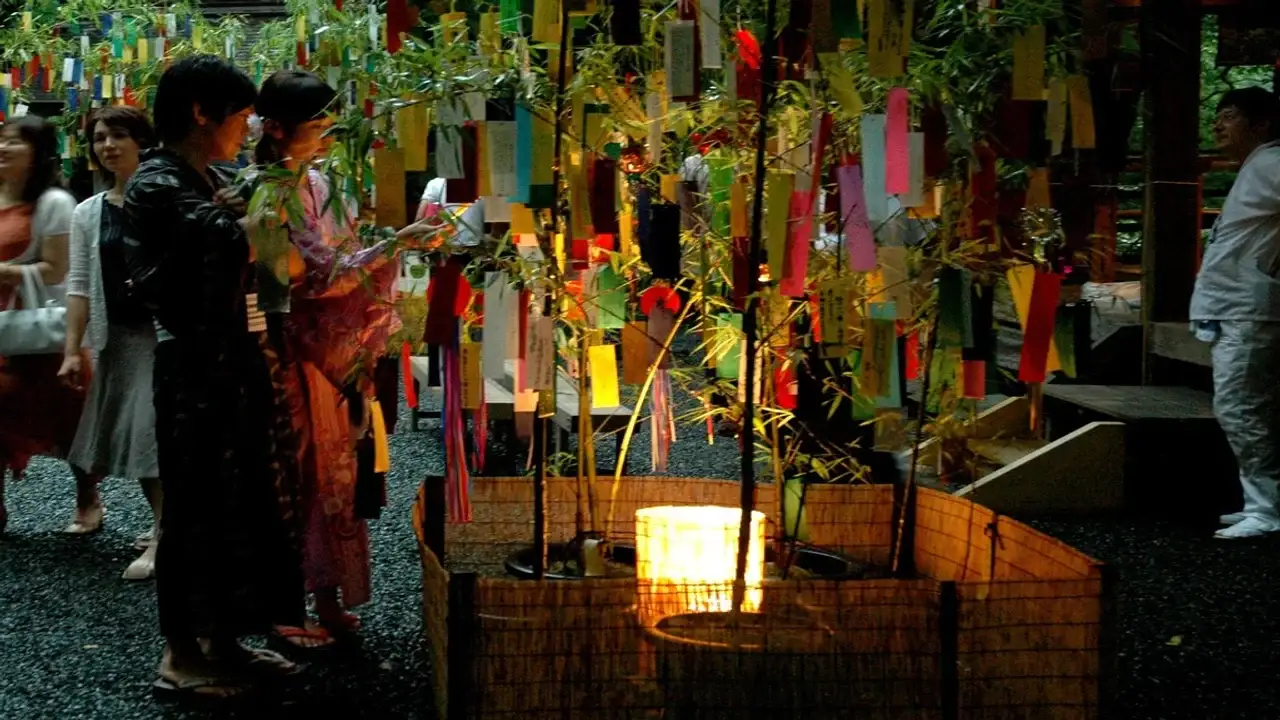 Personas en yukata colgando tanzaku de colores en ramas de bambú iluminadas durante el Tanabata real en un santuario japonés