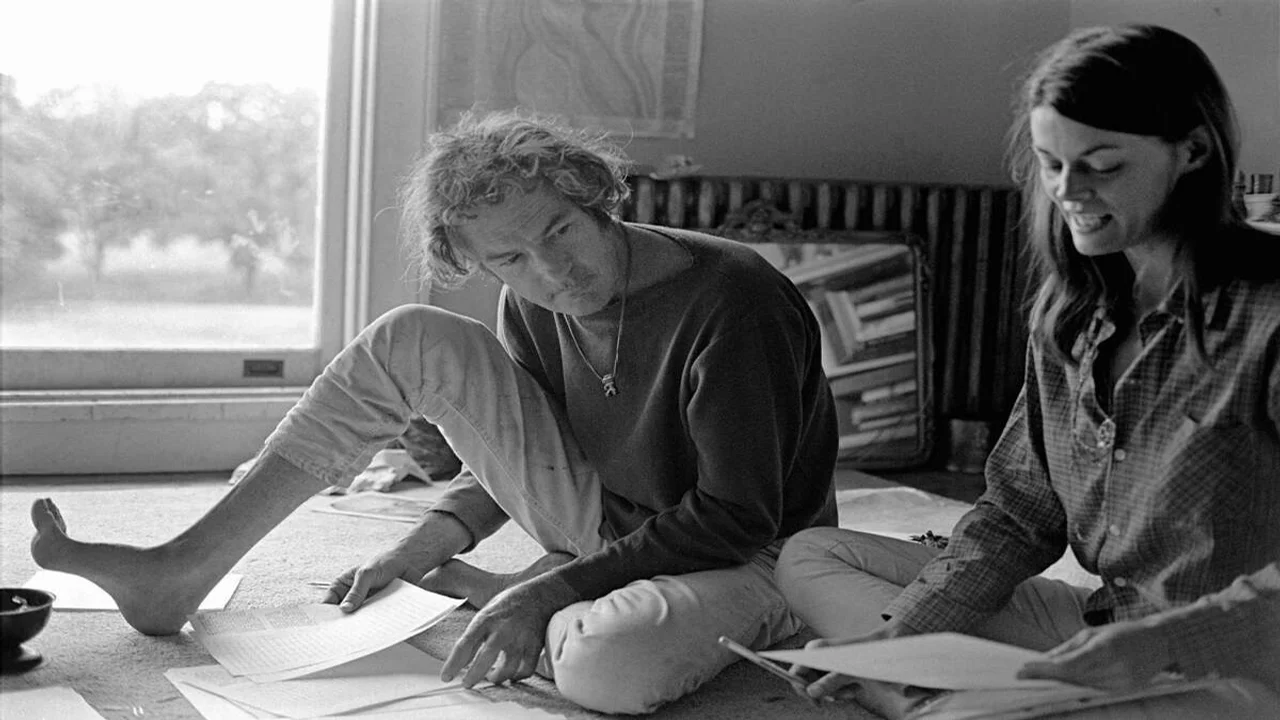 Timothy Leary revisando documentos en el suelo junto a una mujer, fotografía en blanco y negro de los años 70