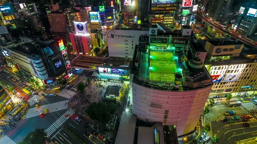 Vista aérea nocturna de Shibuya con campo de fútbol en la azotea de un edificio comercial en Tokio