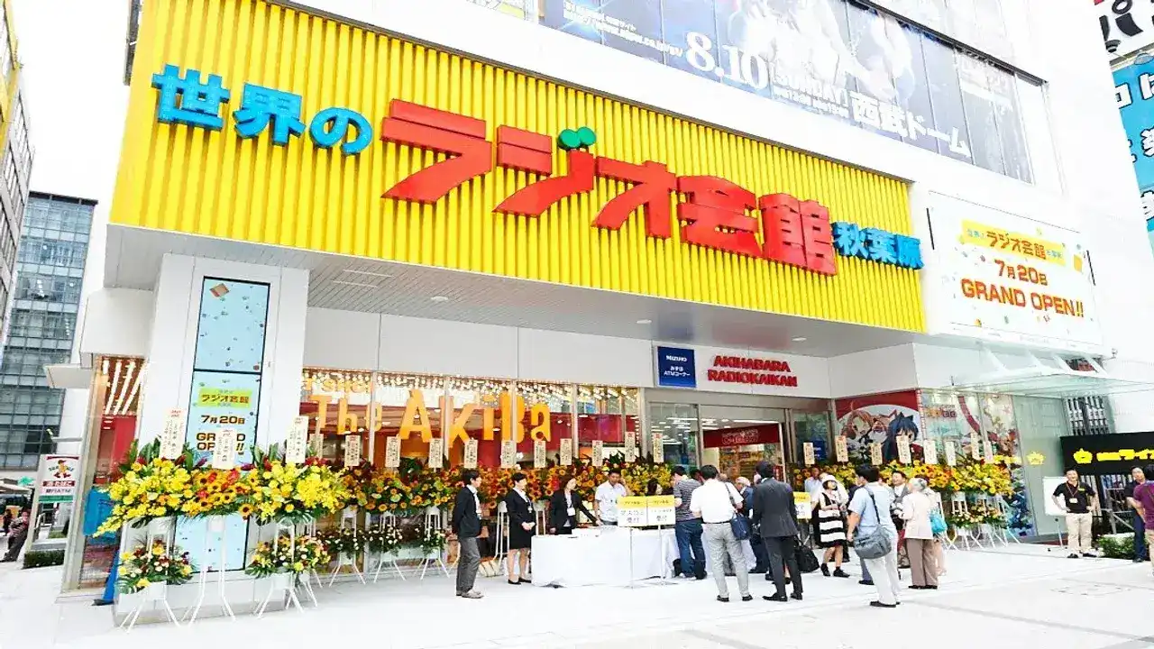 Fachada amarilla del emblemático edificio Akihabara Radio Kaikan en Tokio durante el evento de su gran apertura, decorada con arreglos florales.