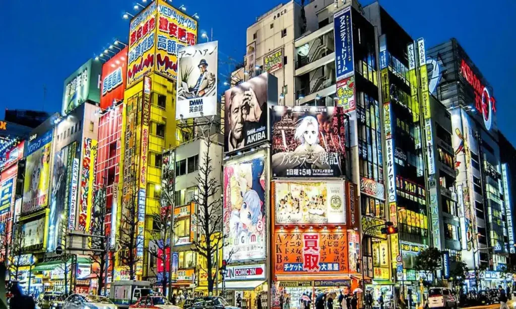 Calle principal de Akihabara de noche, iluminada con coloridos letreros de neón y enormes anuncios de anime y videojuegos en Tokio.