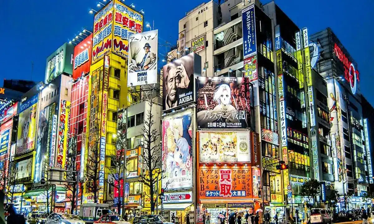 Calle principal de Akihabara de noche, iluminada con coloridos letreros de neón y enormes anuncios de anime y videojuegos en Tokio.