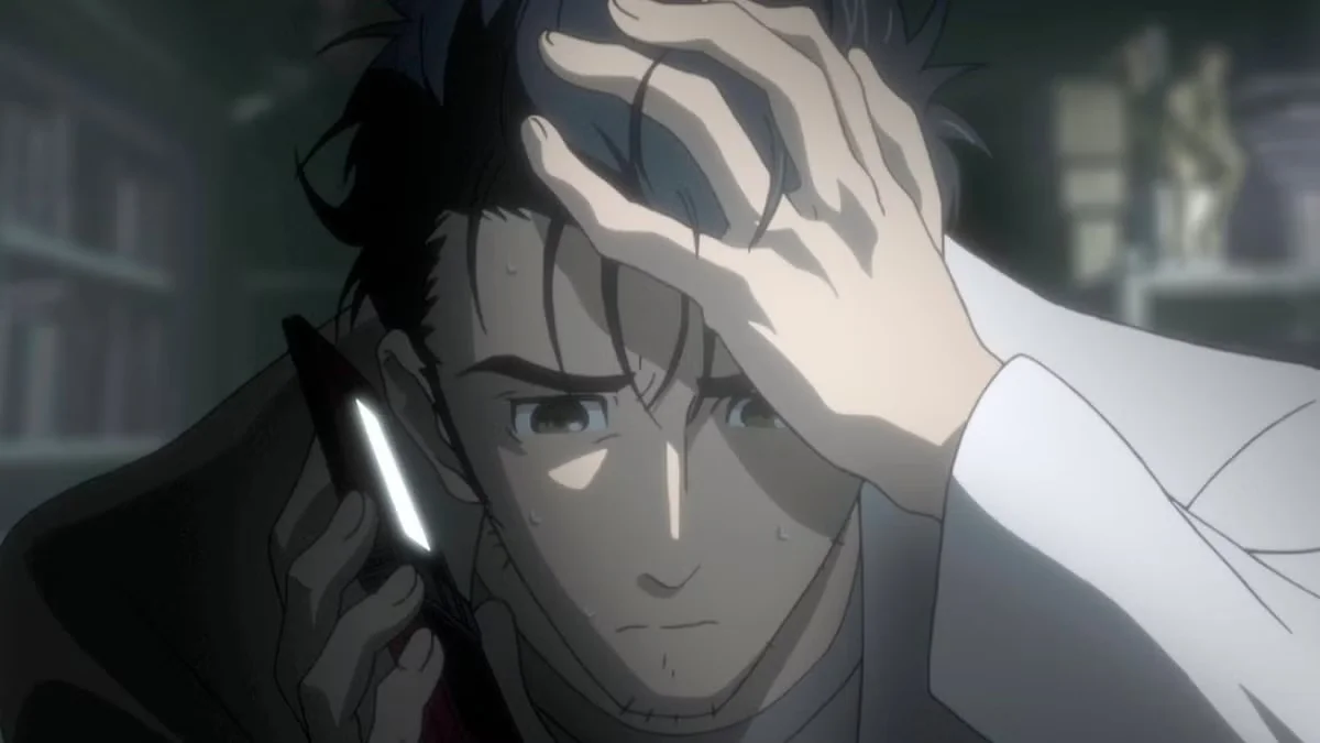 Rintaro Okabe con expresión de angustia y mano en la frente hablando por teléfono, escena de tensión en Steins;Gate
